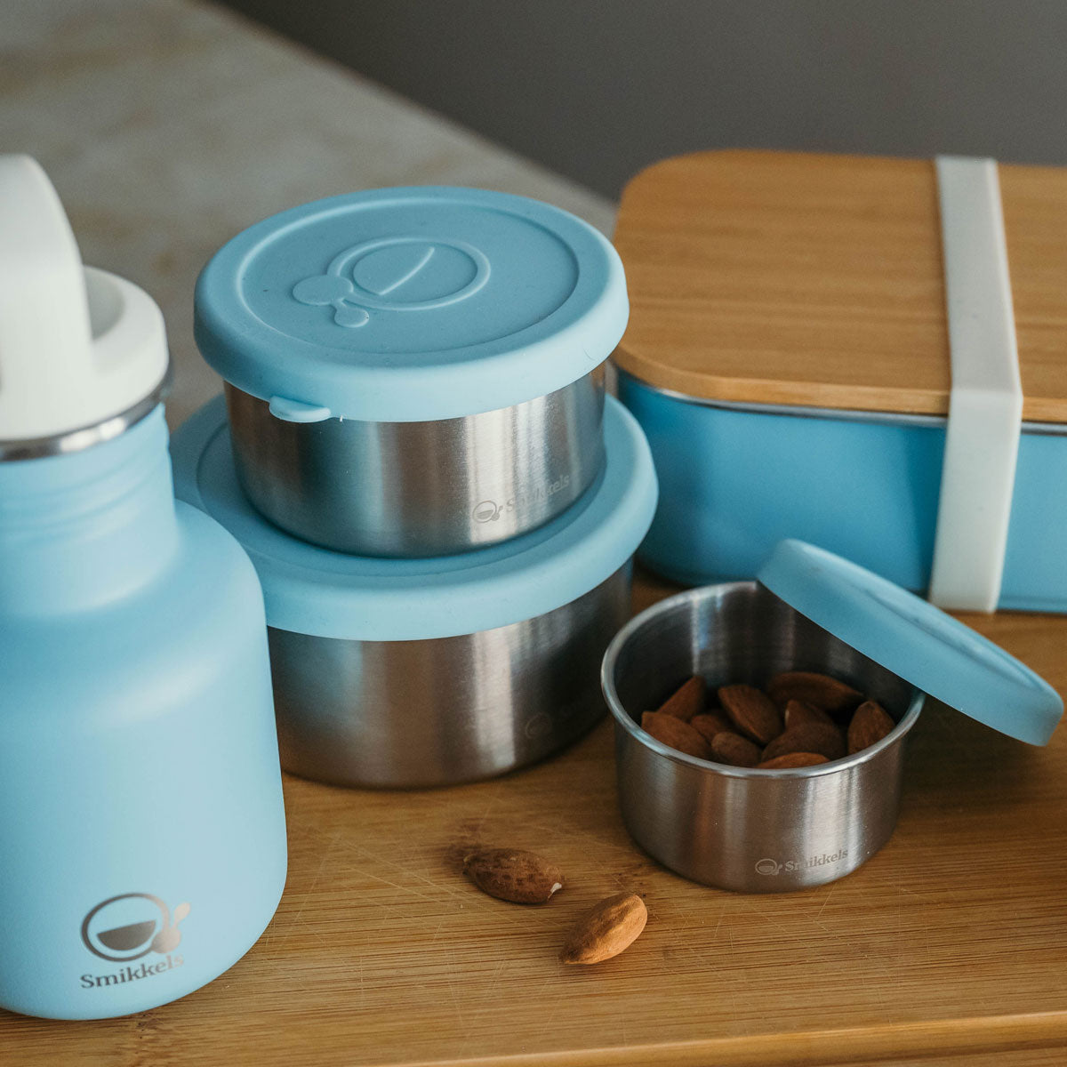 Blauwe fruit- en snackbakjes op een houten plank met bijpassende drinkfles en lunchbox