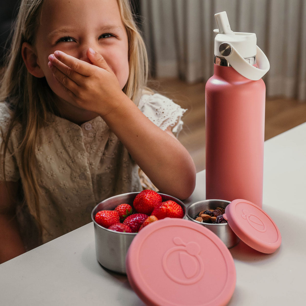 Meisje lacht bij roze fruit- en snackbakjes met nootjes en aardbeien en roze thermos drinkfles