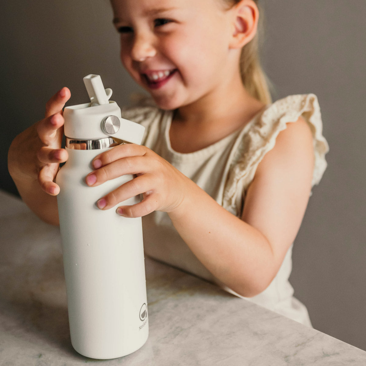 Lachend meisje opent witte thermos drinkfles