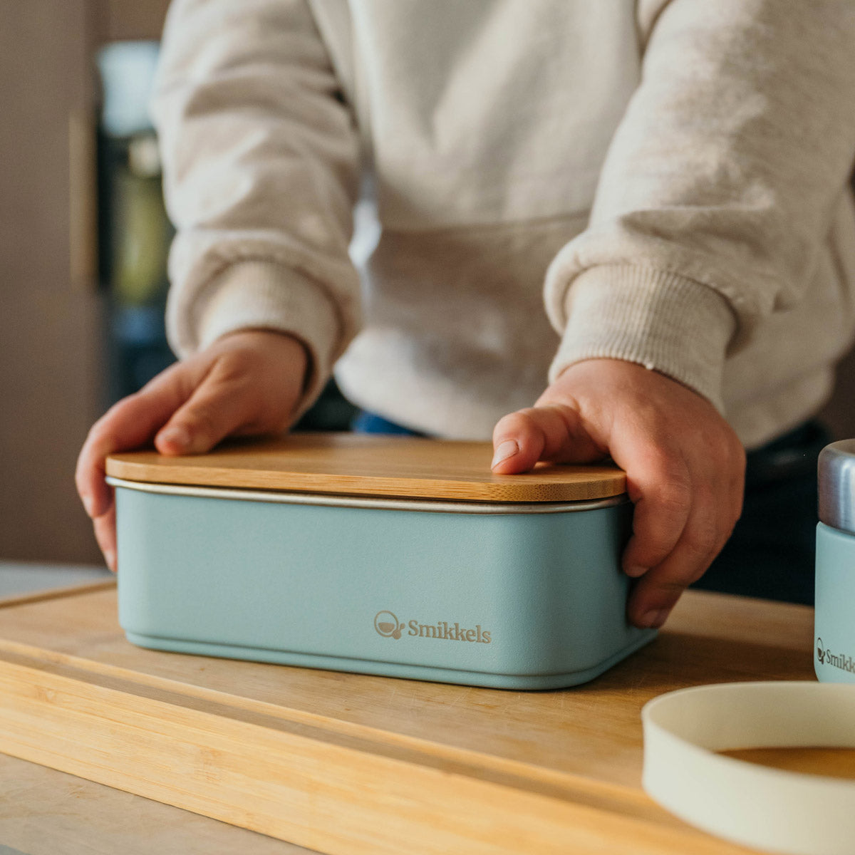 Kind drukt bamboe deksel dicht van blauwe RVS Smikkels lunchbox