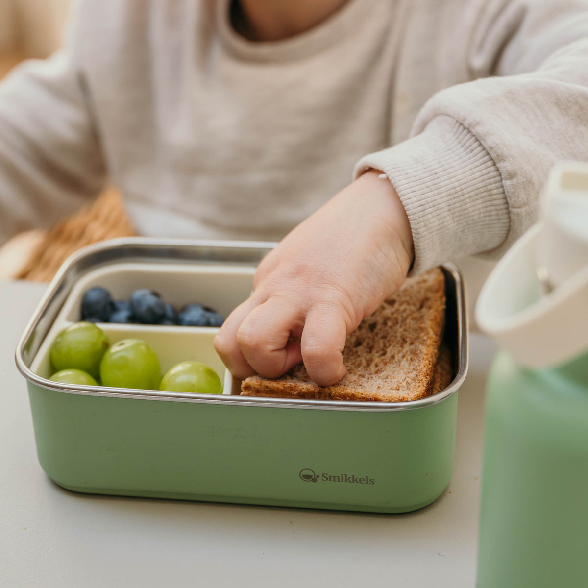 kind haalt boterham uit groene RVS lunchbox van Smikkels