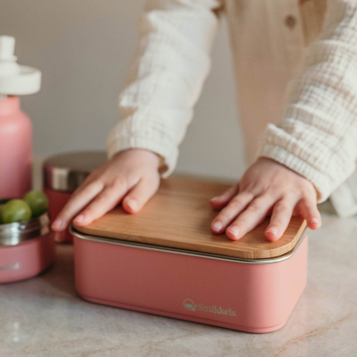 Kind drukt bamboe deksel op roze RVS Lunchbox van Smikkels