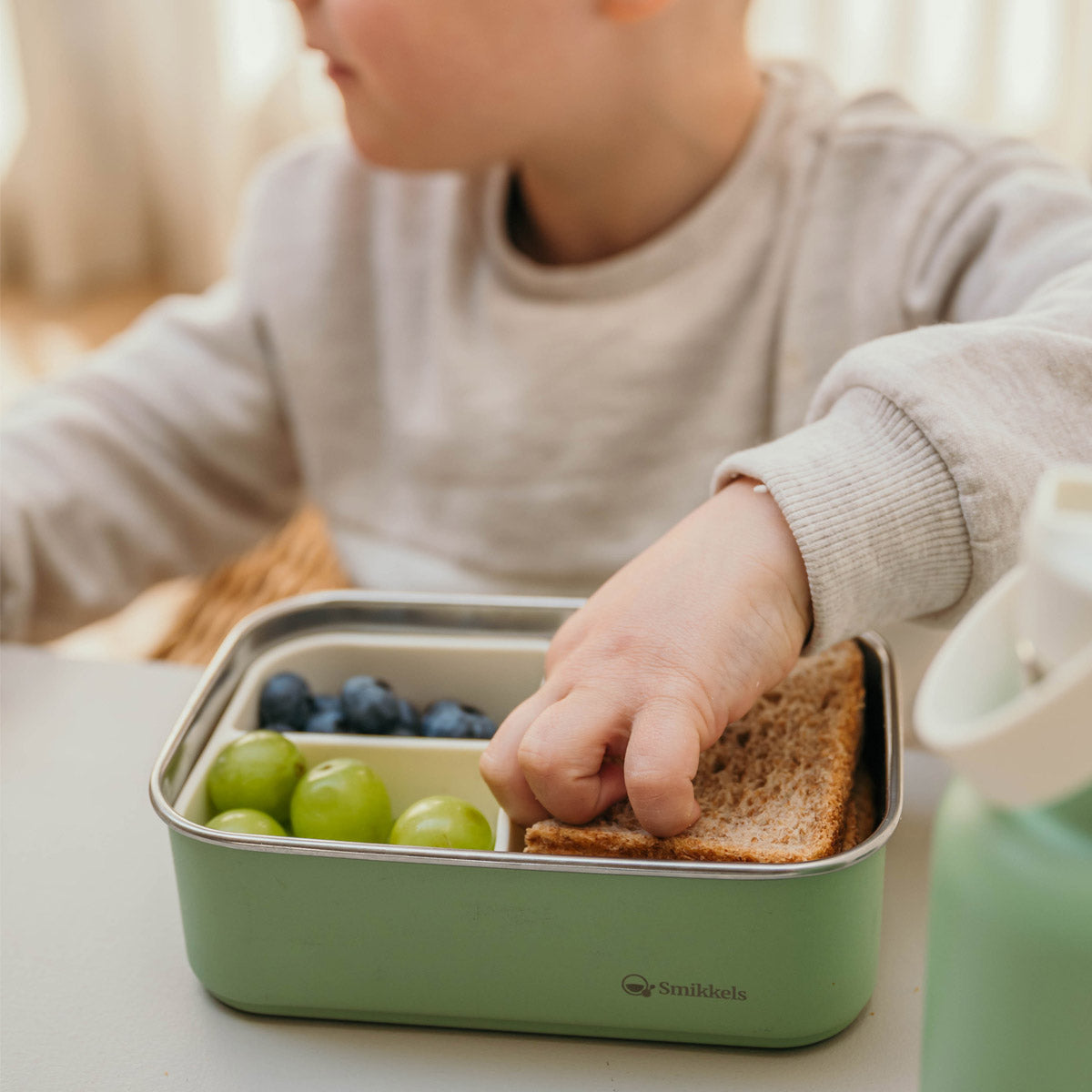 Jongetje pakt iets uit een gevulde groene rvs lunchbox met verdeler