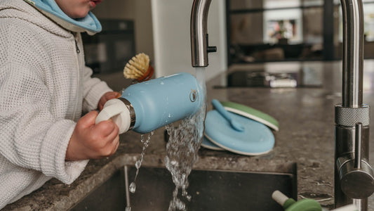 Kind spoelt een blauwe rvs drinkfles van Smikkels om onder de kraan in de keuken