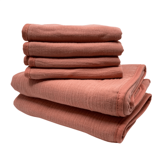 Een stapel van roze monddoekjes en babyhanddoeken van Smikkels met een grote rode strik er bij