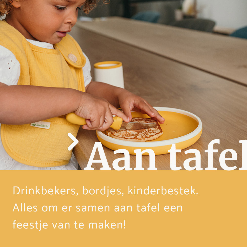 Kind met gele slab dat een pannekoek snijdt op een geel siliconen bordje van Smikkels