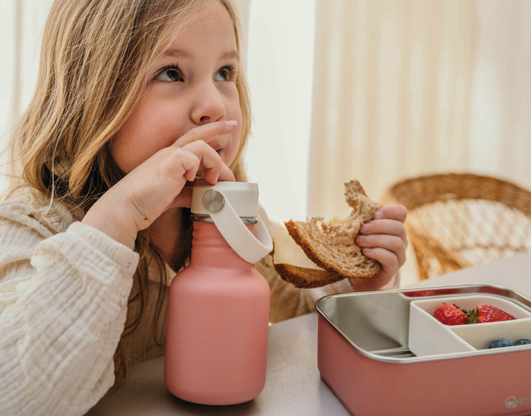 Meisje aan tafel met roze RVS drinkfles en lunchbox van Smikkels, klaar voor de eerste schooldag – Back to School