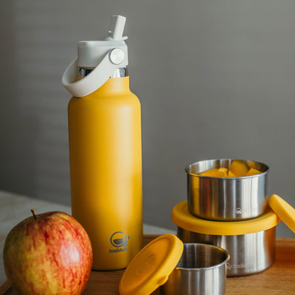 Gele thermos drinkfles op plank met snackbakjes en appel