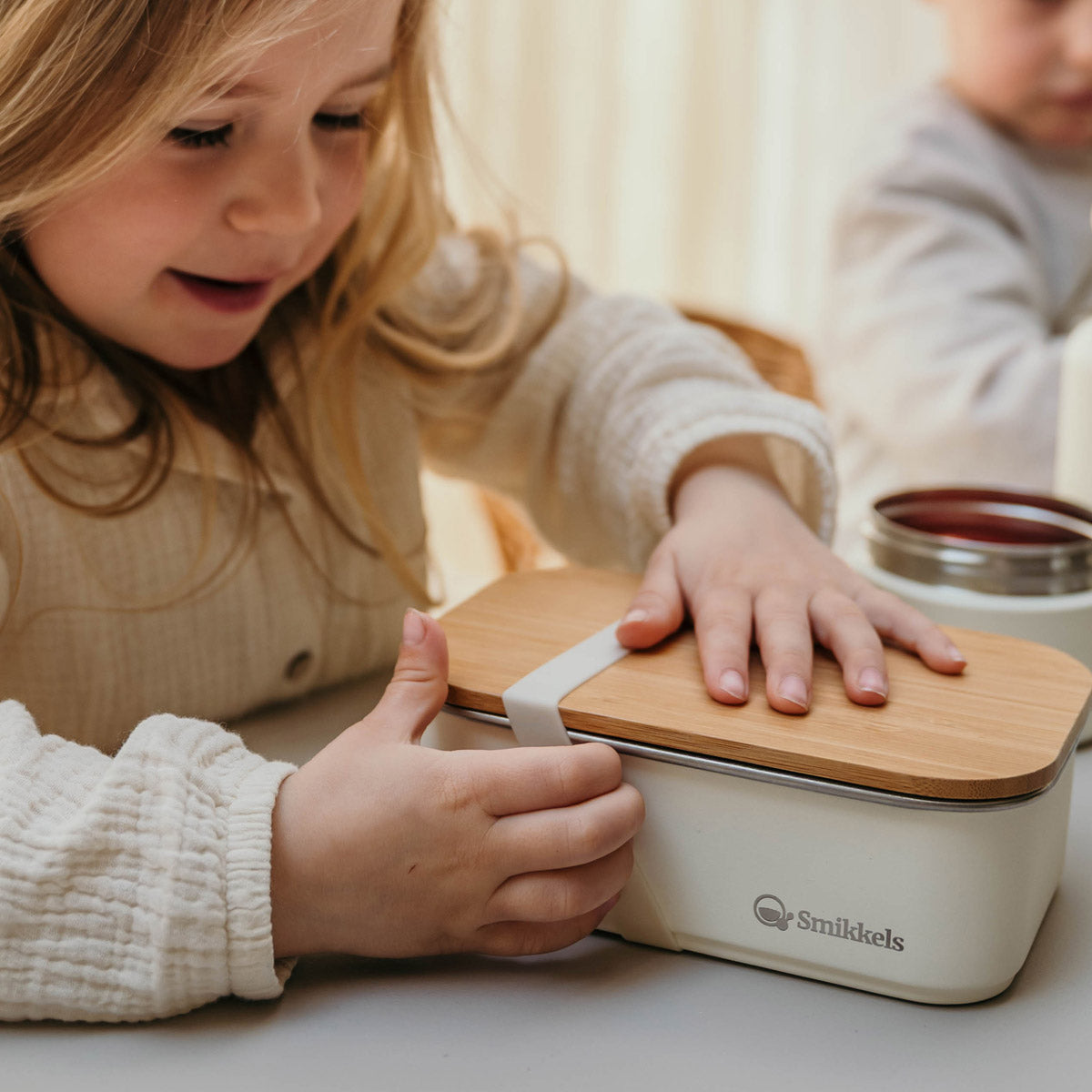 Meisje trekt aan elastiek van witte RVS Smikkels lunchbox