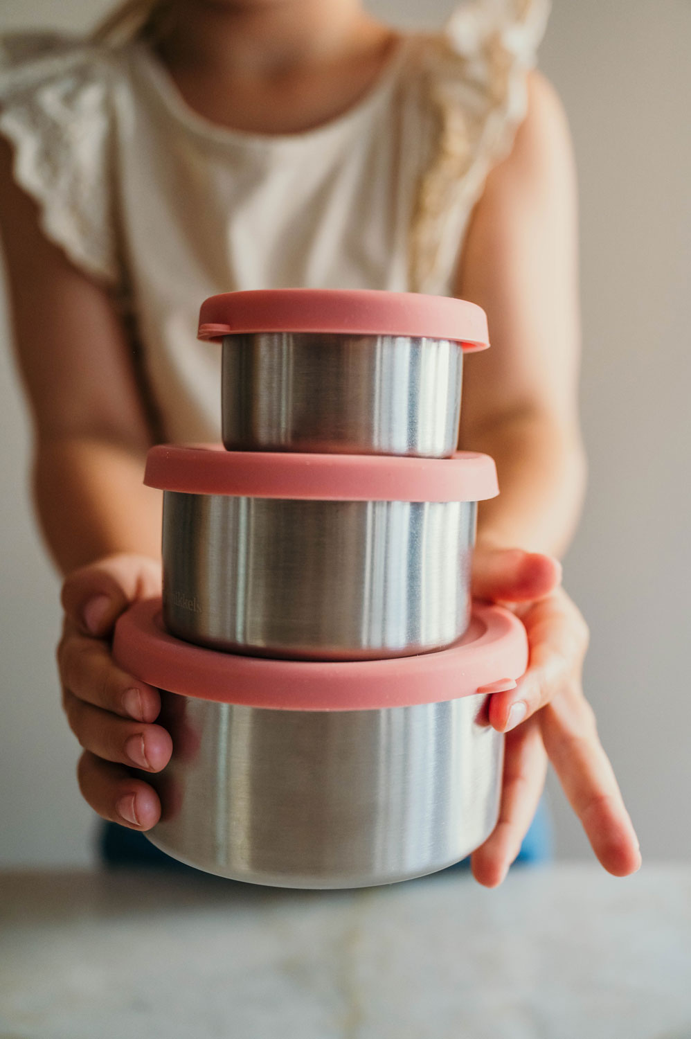Stapen RVS voedselbewaarbakjes met roze silicone deksels van Smikkels, vastgehouden door een meisje