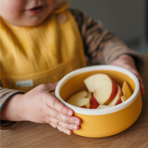 Geel siliconen kommetje van Smikkels met stukjes appels, vastgehouden door een jongetjes met een geel slabbetje