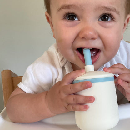 Vrolijk kind met siliconen drinkbeker met rietje. Blauw rietje en witte beker met blauwe rand - Smikkels