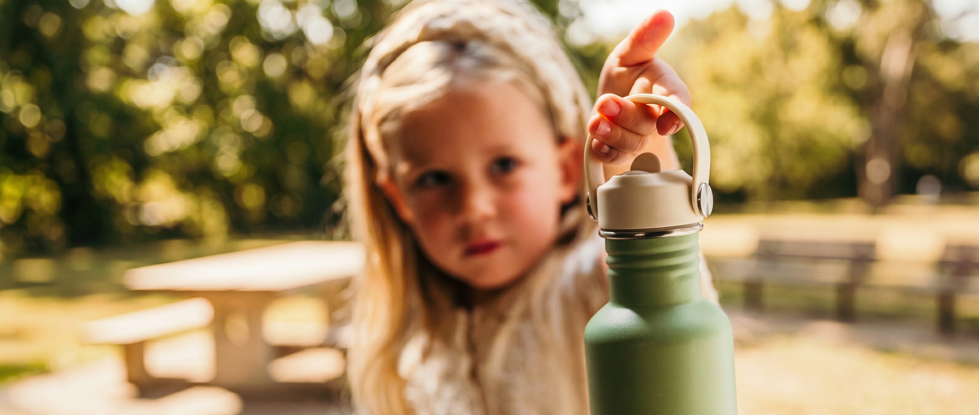 Meisjes houdt in de buitenlucht een groene drinkfles van Smikkels omhoog